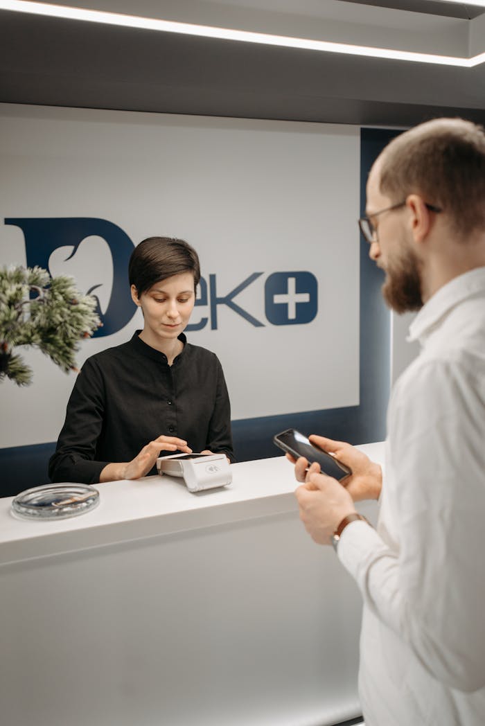 Customer making a cashless payment at a clinic reception using a smartphone and a wireless terminal.